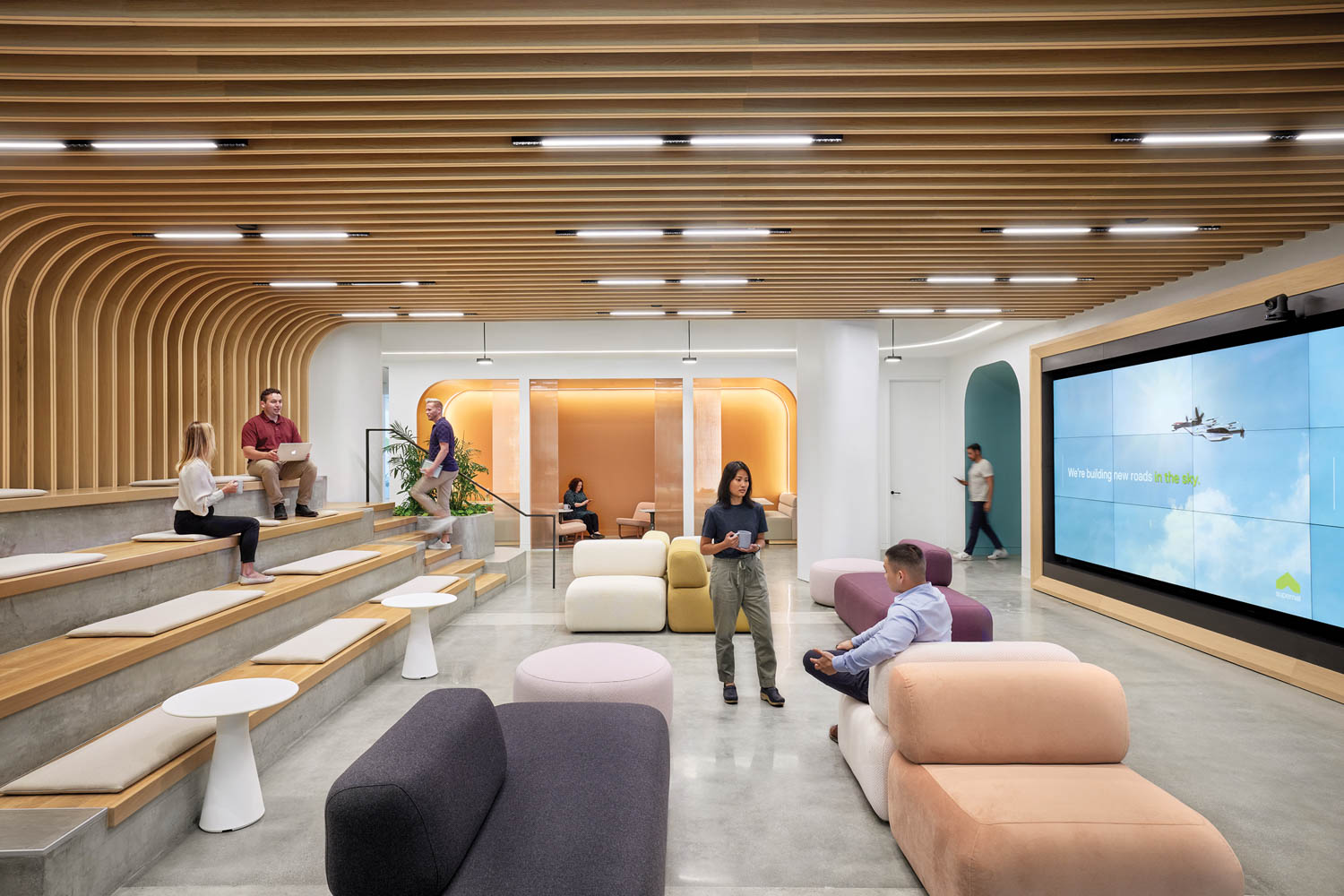 multi-use space with custom soft seating in different colors, screens and slatted ceiling